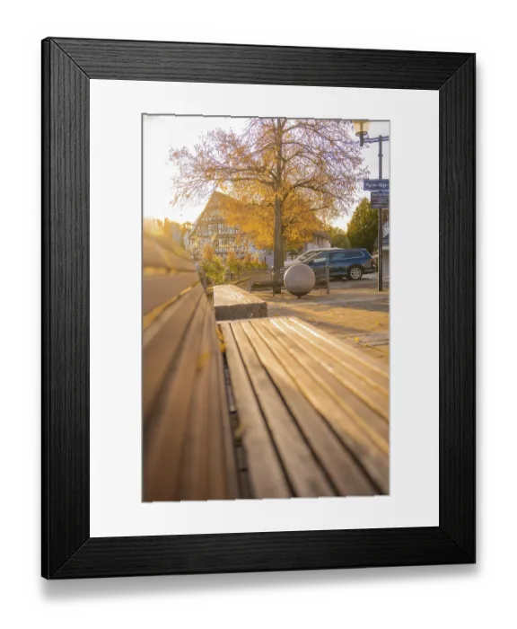 Framed Print : Empty wooden bench in a sunlit village square with half-timbered house in the background