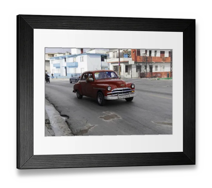 Framed Print : Red vintage car on a grey road with surrounding urban-style buildings