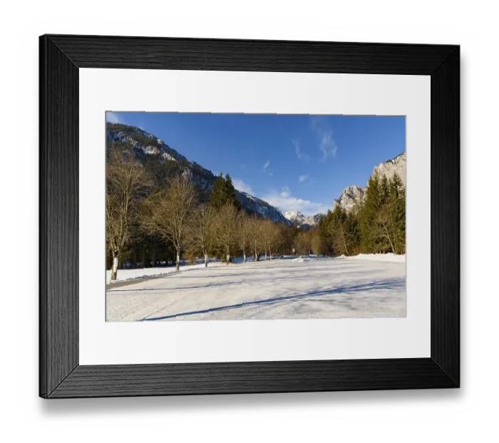 Framed Print : A scenic winter view featuring a snow-covered road flanked by bare trees with mountains in the background