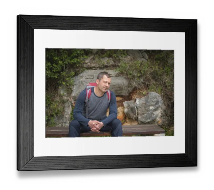 Framed Print : Caucasian male with a backpack pausing to rest on a bench while walking on a path in a forest on a coastal trail