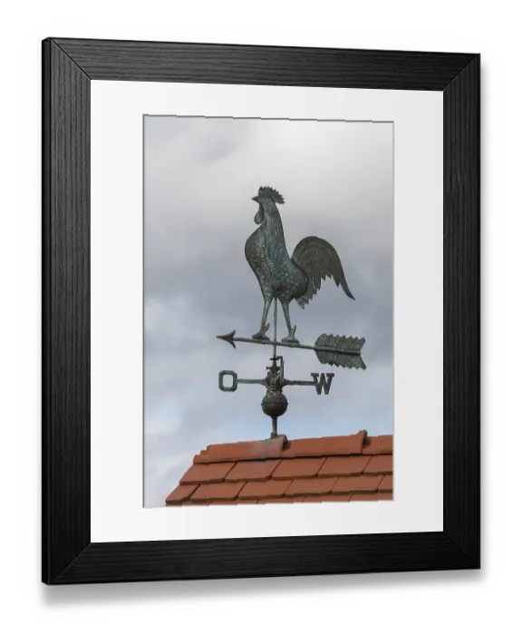 Framed Print : Metal weather vane with rooster on a tiled roof against cloudy sky