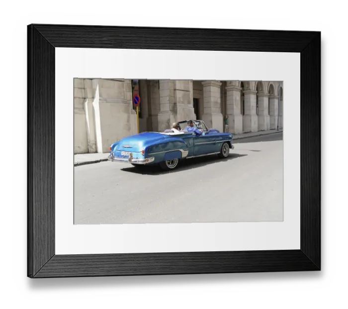 Framed Print : Blue convertible drives past a historic building
