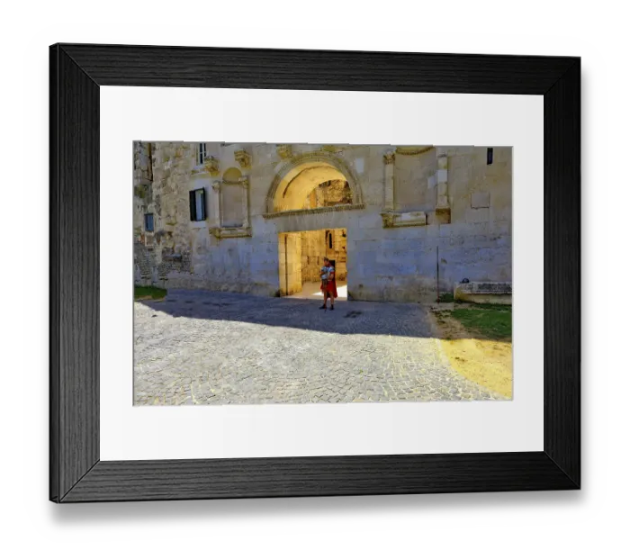 Framed Print : Monumental stone gate with round arch and cobblestones in bright sunshine