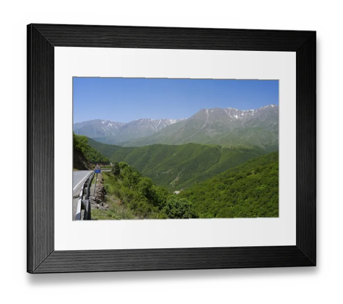 Framed Print : A winding mountain road snakes through green hills with mountains in the background Framed Print : A winding mountain road snakes through green hills with mountains in the background