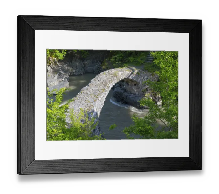Framed Print : An old stone bridge spans a river amid green trees and rocks