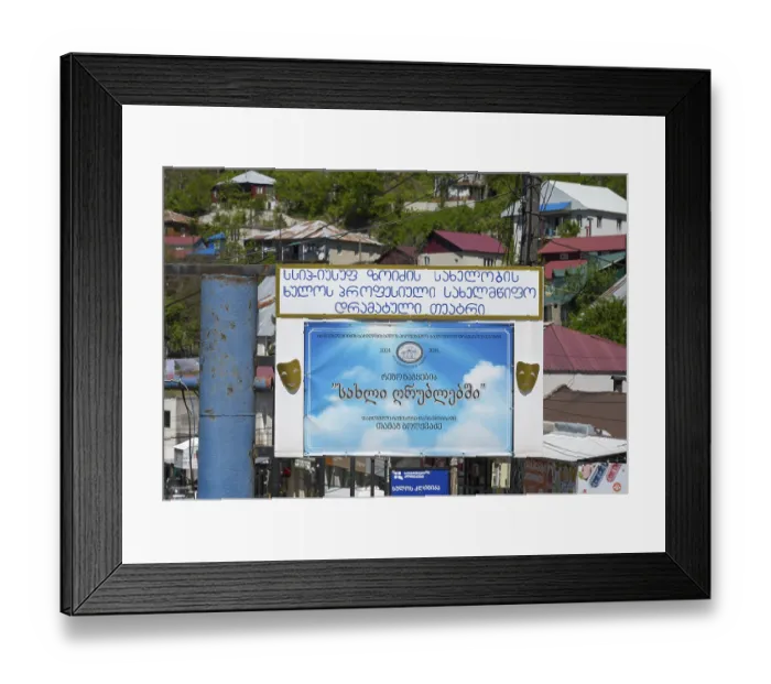 Framed Print : A large advertising sign with a blue poster and text surrounded by colorful buildings and green trees