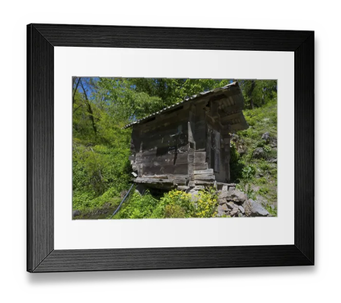 Framed Print : An old wooden hut stands on a rocky hill surrounded by green vegetation and wildflowers