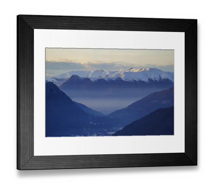 Framed Print : Misty valley lies beneath snow-capped mountain peaks at dusk near Piani di Bobbio in Italy