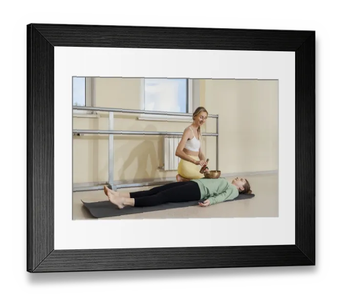 Framed Print : An instructor uses a singing bowl to provide sound therapy to a relaxed participant lying on a mat in a bright studio