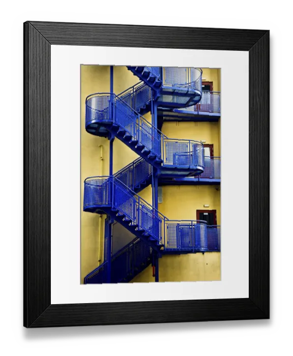 Framed Print : Blue metal fire escape staircases against a yellow wall creating a stark industrial contrast
