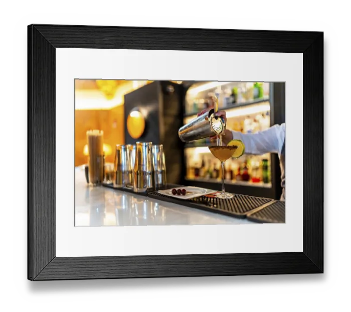 Framed Print : Hand of a waiter filling cocktail into martini glass garnished with lemon in the counter of a luxury night club