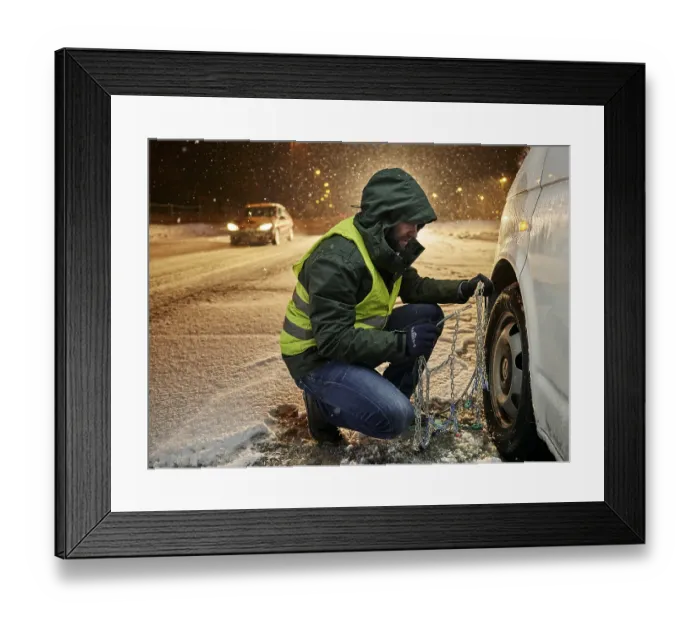 Framed Print : Man with safety vest applying snow chains on snow-covered road Framed Print : Man with safety vest applying snow chains on snow-covered road