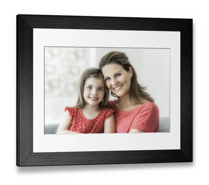 Framed Print : Mother and daughter sit together on the couch and look into the camera Framed Print : Mother and daughter sit together on the couch and look into the camera
