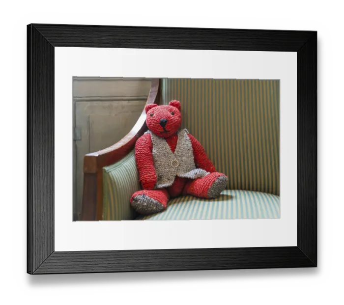 Framed Print : Knitted red teddy bear with vest on striped armchair