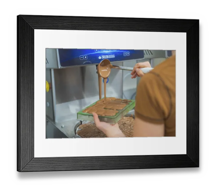Framed Print : Chocolate is filled into flat molds by a person from a device Framed Print : Chocolate is filled into flat molds by a person from a device