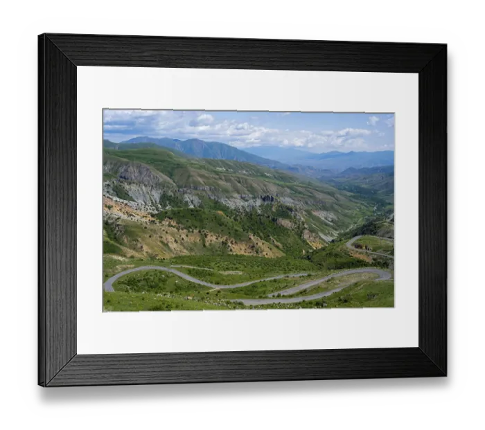 Framed Print : A winding road winds through the green mountains under a blue sky