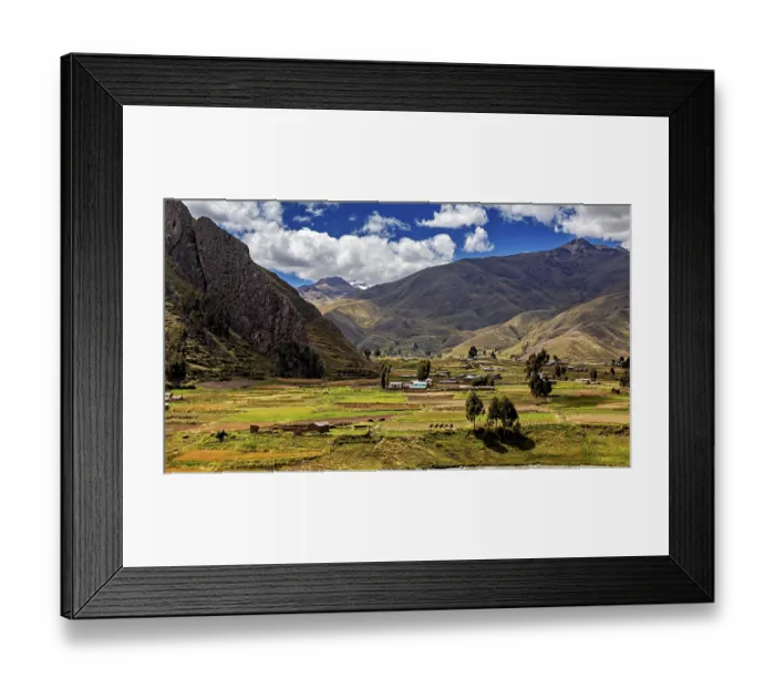 Framed Print : Green fields and hills against a mountain backdrop under a cloudy blue sky Framed Print : Green fields and hills against a mountain backdrop under a cloudy blue sky