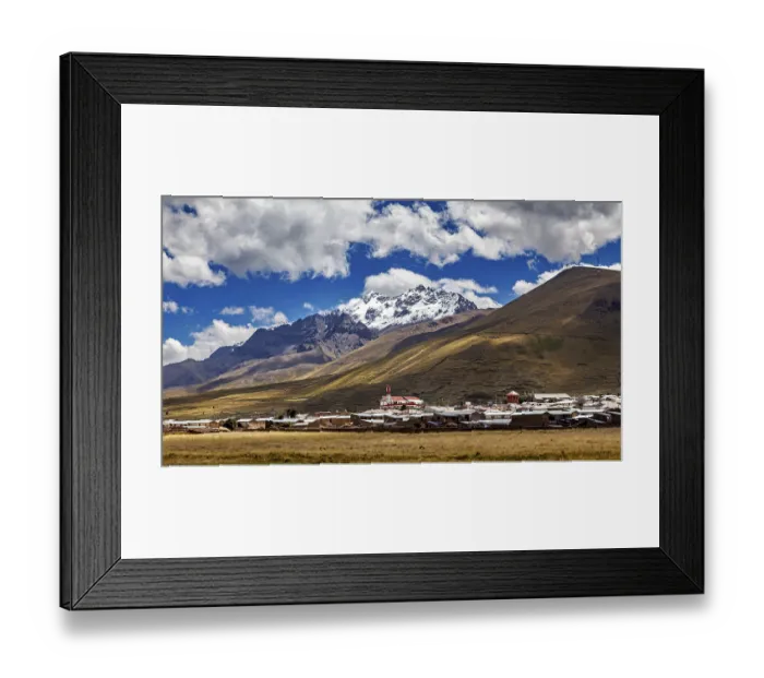 Framed Print : A village at the foot of snow-capped mountains under a blue sky with clouds
