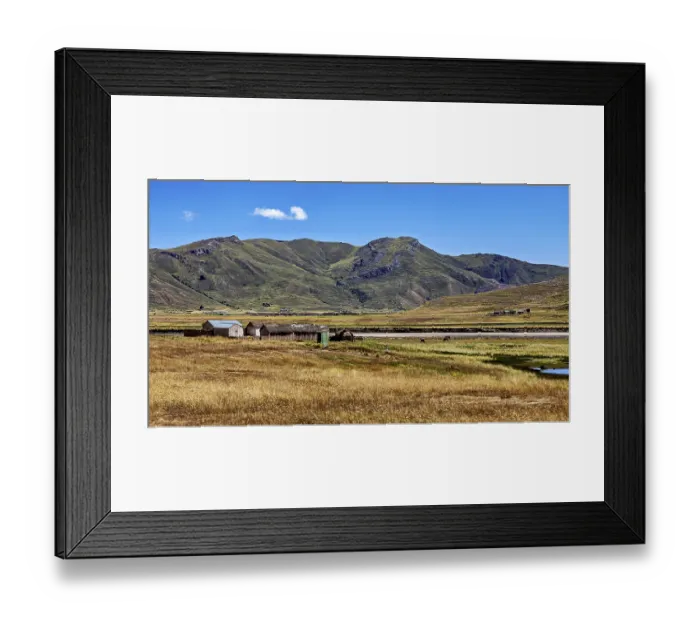 Framed Print : Small houses in front of a hill and mountain landscape under a blue sky