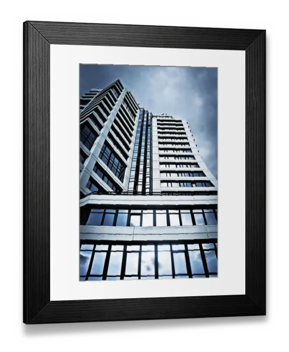 Framed Print : A tall, modern building with glass windows against a cloudy sky Framed Print : A tall, modern building with glass windows against a cloudy sky