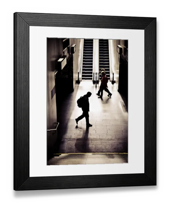 Framed Print : Silhouettes of people walking in a dimly lit subway station with prominent shadows and stairs