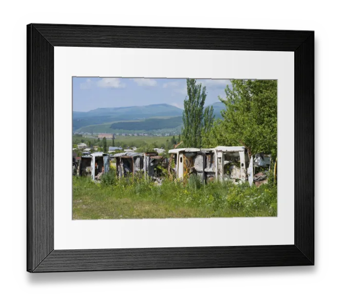 Framed Print : Row of rusty cars in a meadow with green trees and mountains