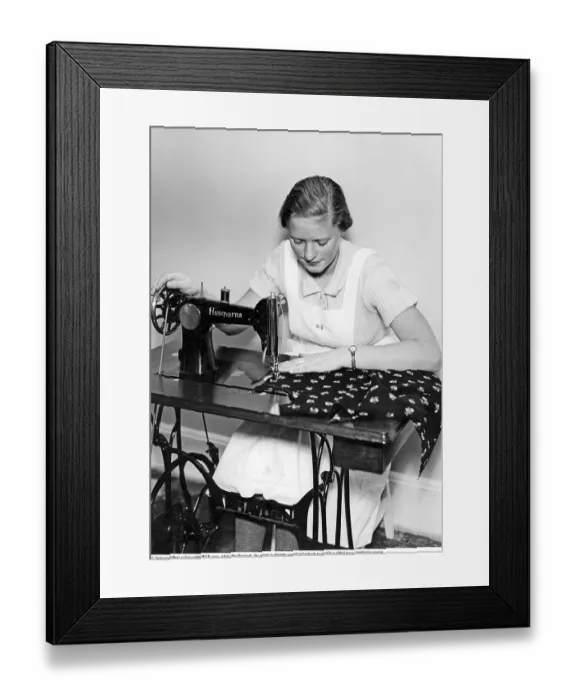 Framed Print : A young woman sits sewing at a Husqvarna sewing machine in the 1930s