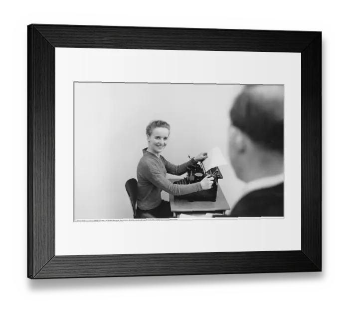 Framed Print : Office worker in the 1950s. She sits at a typewriter in an office Framed Print : Office worker in the 1950s. She sits at a typewriter in an office