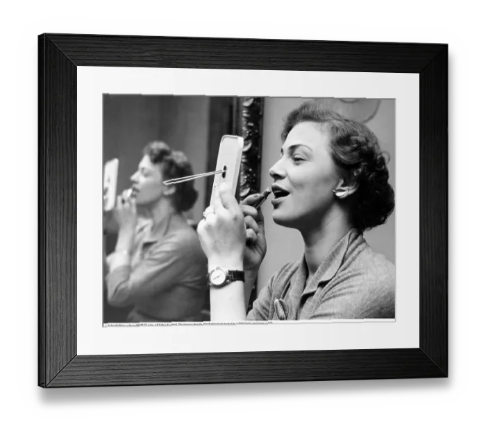 Framed Print : Looking good in the 1950s. She is looking at herself in the pocket mirror while applying lipstick