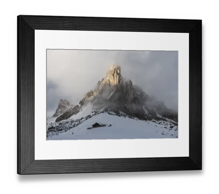 Framed Print : A hut is located under huge, snow-covered mountain peaks and clouds on Passo di Giau