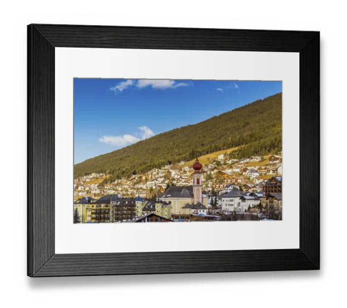 Framed Print : Snowy alpine village in Italy illuminated by sun with mountains in the background