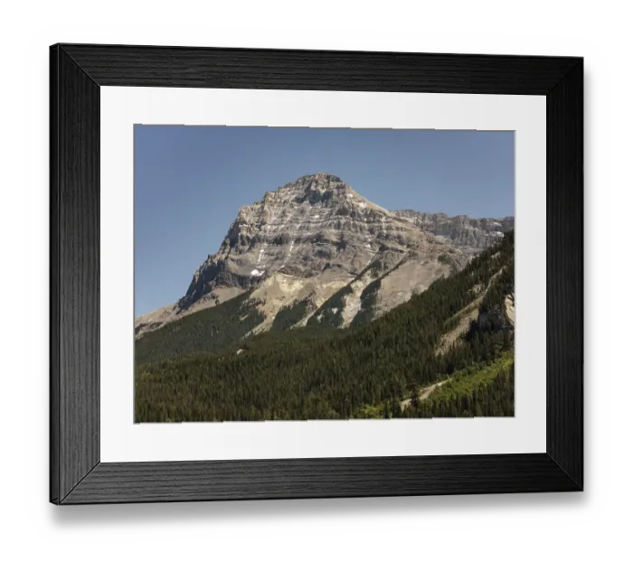 Framed Print : Majestic mountain peak with rocky slopes towering over a dense forest under a clear sky in British Columbia