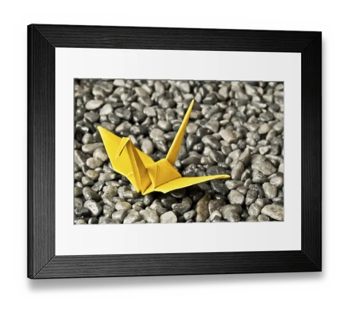 Framed Print : A yellow origami crane sits on a bed of gray pebbles