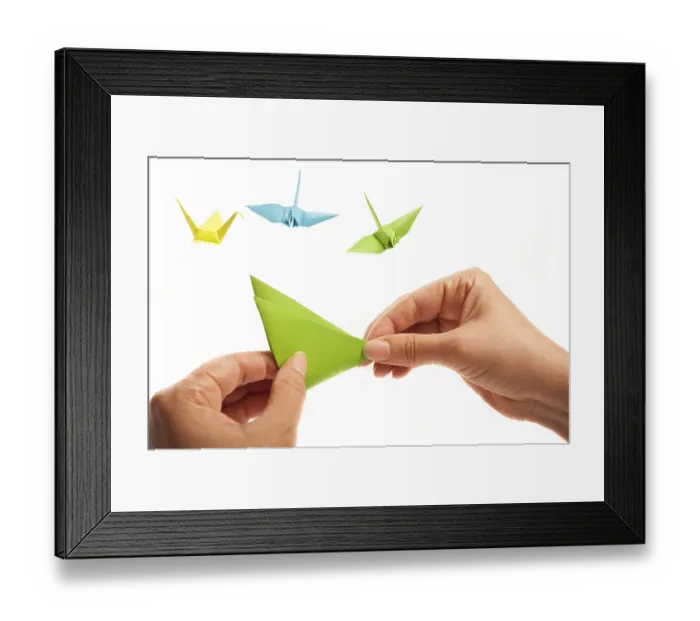 Framed Print : Hands crafting an origami piece with colorful cranes in the background