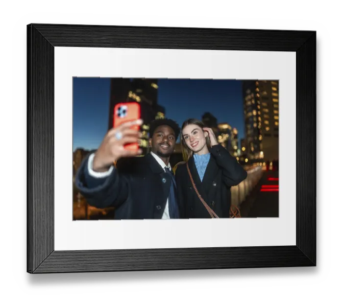 Framed Print : Diverse couple happily capturing a moment together using a mobile device for a selfie