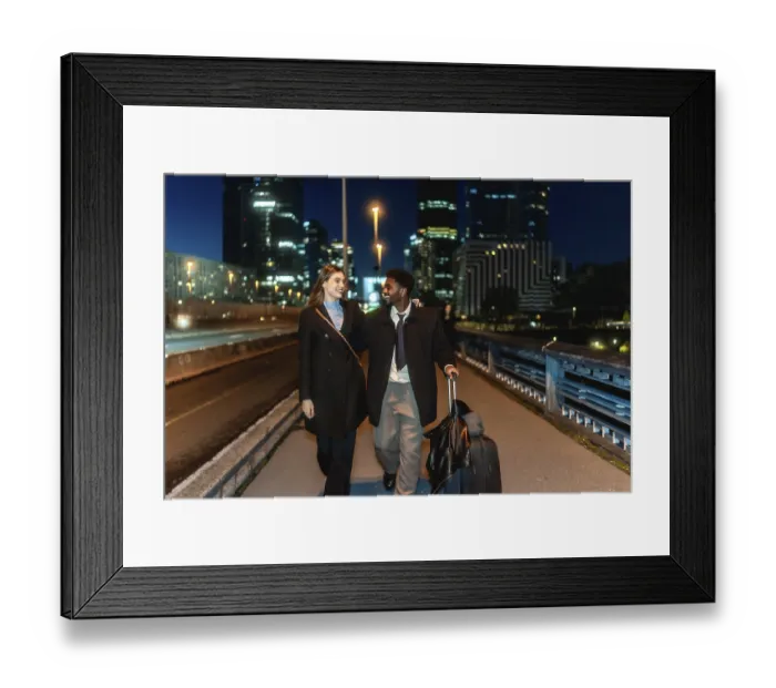 Framed Print : Diverse couple walking together holding hands and pulling a suitcase in a modern urban city district at night Framed Print : Diverse couple walking together holding hands and pulling a suitcase in a modern urban city district at night