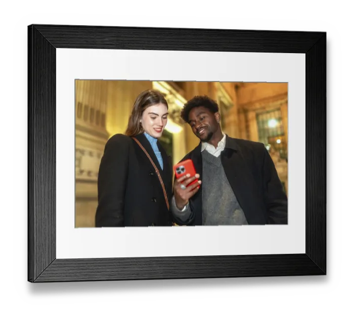 Framed Print : Diverse couple standing close, looking at a smartphone screen and smiling Framed Print : Diverse couple standing close, looking at a smartphone screen and smiling