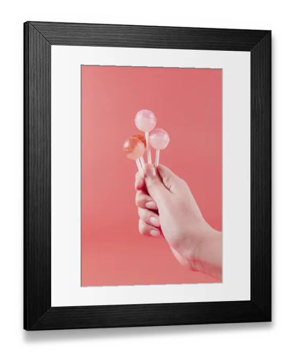 Framed Print : Close up womans hand holding lollipops against coral backdrop