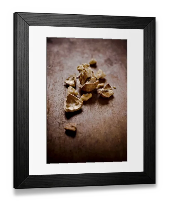 Framed Print : Cracked walnut shells and pieces scattered on a rustic wooden surface