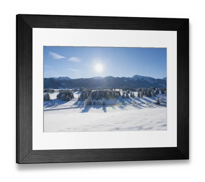 Framed Print : Snow-covered landscape with bright sun over mountains and trees