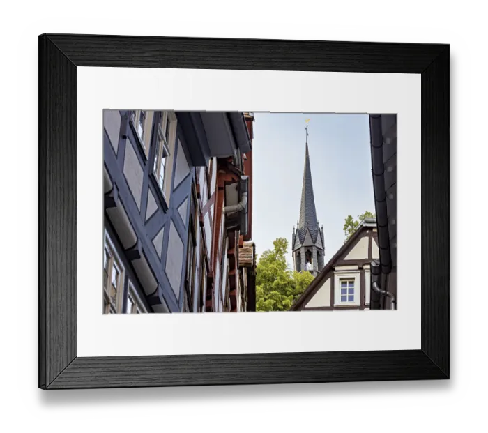 Framed Print : View of a narrow street with half-timbered houses and a church tower in the background Framed Print : View of a narrow street with half-timbered houses and a church tower in the background