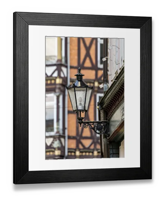 Framed Print : Nostalgic lantern in front of a half-timbered house with distinctive architectural patterns and windows