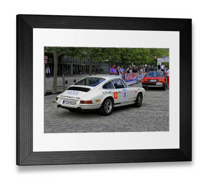 Framed Print : A white Porsche classic car with racing stickers drives through a city street with trees and spectators Framed Print : A white Porsche classic car with racing stickers drives through a city street with trees and spectators