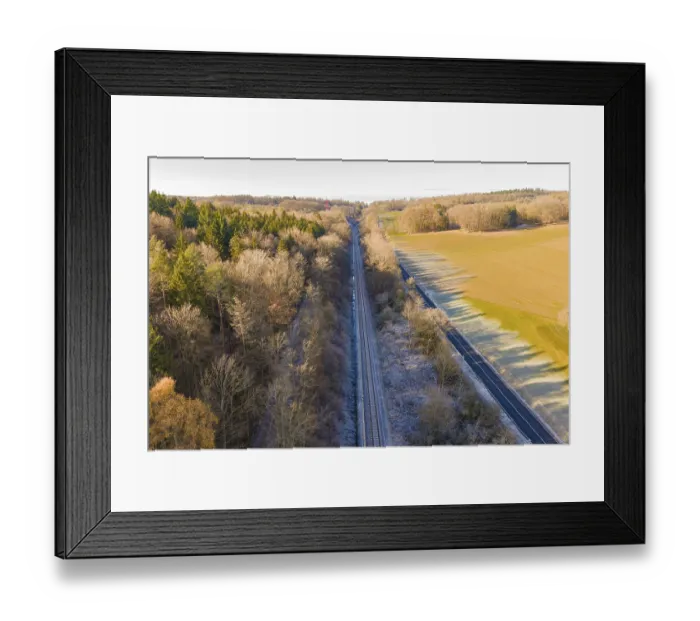 Framed Print : Railway line between trees and a country road surrounded by nature Framed Print : Railway line between trees and a country road surrounded by nature