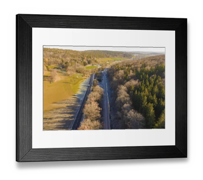 Framed Print : Aerial view of a railway line between trees and a road in a rural area