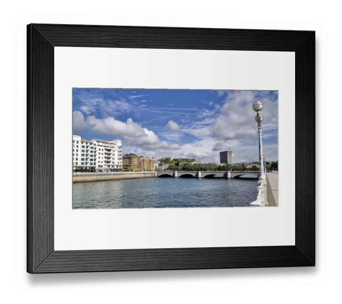Framed Print : Wide view of a city bridge with river and surrounding buildings under a blue sky Framed Print : Wide view of a city bridge with river and surrounding buildings under a blue sky