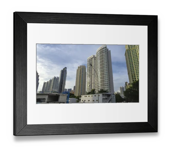Framed Print : Modern skyscrapers rise into the sky of a city surrounded by trees and clear blue sky