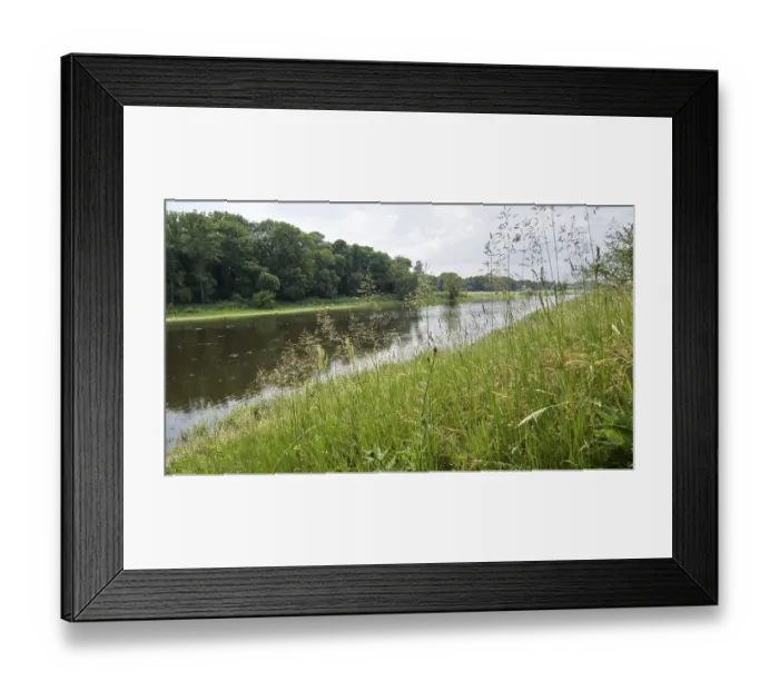 Framed Print : River course with grassy bank and forest in the background under a cloudy atmosphere Framed Print : River course with grassy bank and forest in the background under a cloudy atmosphere