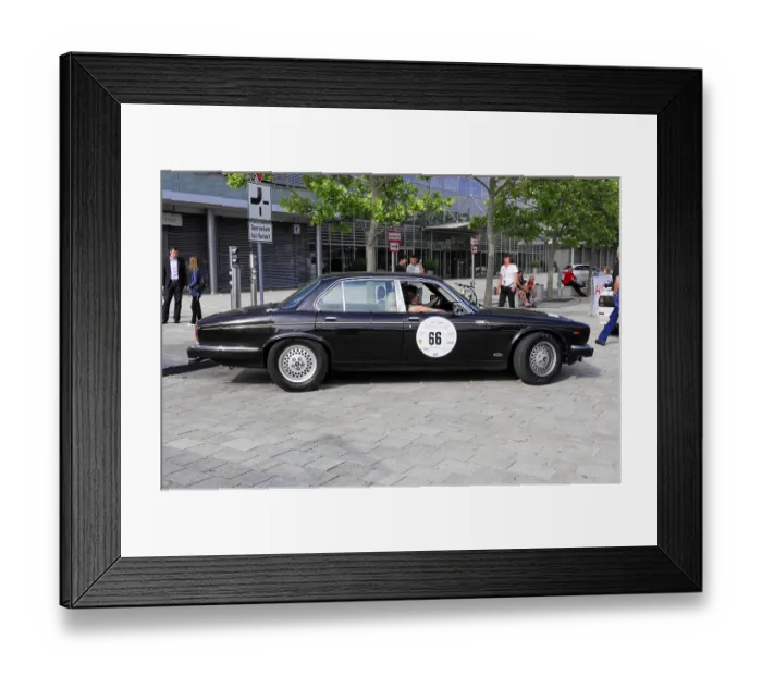 Framed Print : Black vintage limousine with number 66 in an urban setting with trees and people