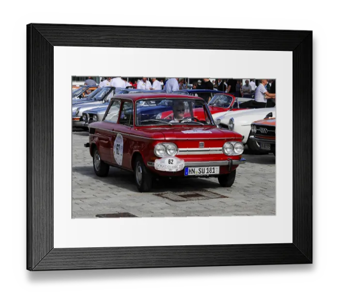 Framed Print : Red nostalgic vintage small car on street with driver surrounded by people